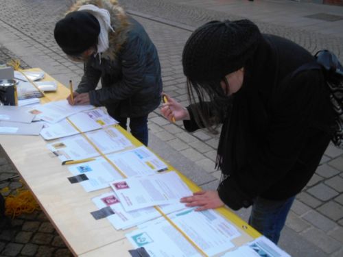 Menschen unterschreiben Petitionen an einem Stand zum Briefmarathon in der Fußgängerzone.